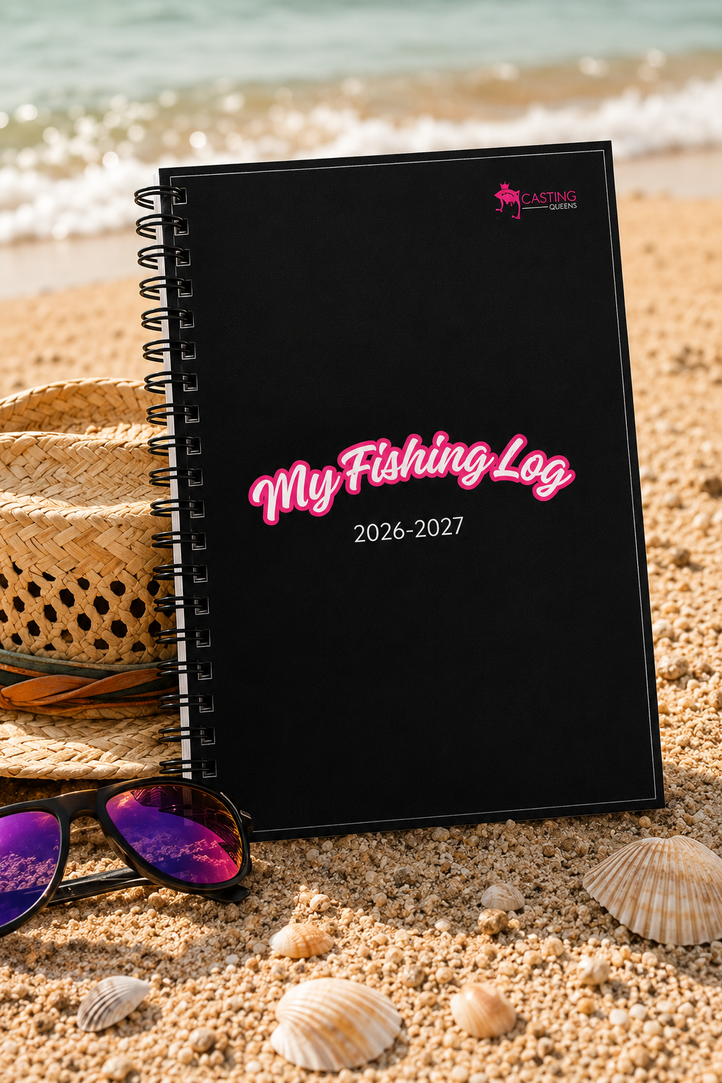 Casting Queens My Fishing Log 2026–2027 spiral-bound fishing journal on a sandy beach.